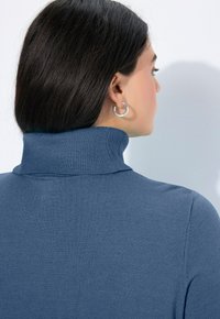 Sininen poolopaita, joka on valmistettu neulotusta kankaasta ja jossa on ribbireuna. Ominaisuuksiin kuuluu sileä rakenne ja istuva siluetti, kuvattu takaa.