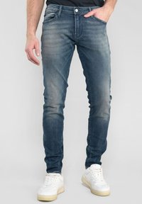 Strakke donkerblauwe denim jeans met een lichte vervaging, vijf-pocketontwerp en een rits. Draag het met witte sneakers.