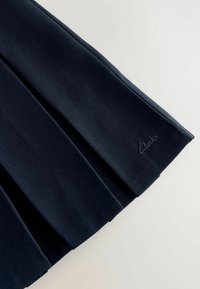 Fald crni od naboranog materijala s teksturiranim završetkom. Ima mali reljefni logotip "Clarks" blizu ruba. Pogodno za formalne prigode.