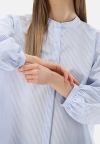 Light blue and white striped button-up shirt with a mandarin collar and puffed sleeves, made from soft fabric. Visible wrist detail.