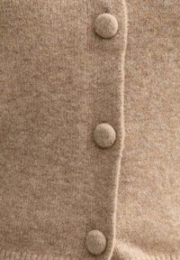 Cardigan beige lavorato a maglia con bottoni rotondi e strutturati lungo una cucitura verticale. Materiale morbido con un motivo sfumato sottile.