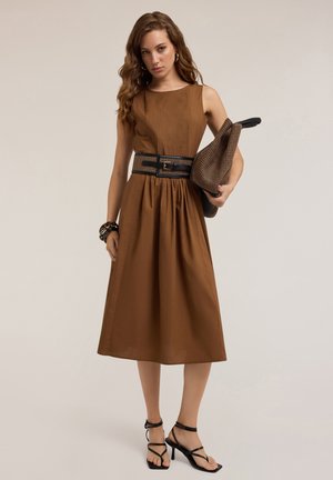Brown midi dress with pleated texture, fitted bodice, and flowy skirt. Paired with a black belt, black strappy sandals, and a textured handbag.