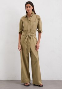Khaki Utility-Overall mit langen Ärmeln, zwei Brusttaschen, tailliertem Gürtel, weitem Hosenbein und durchgehendem Knopfverschluss. Aus glattem Baumwollstoff.