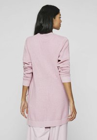 Cardigan lungo rosa con un motivo a maglia testurizzato, polsini a costine e orlo che scende sotto i fianchi. Presenta tasche laterali.