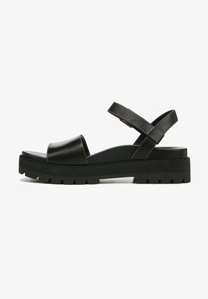 Black leather sandal featuring a wide strap across the toes, a crisscross ankle strap, and a thick rubber platform sole with treads.