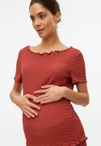 Haut de maternité couleur rouille en tissu texturé et froissé. Présente un col en dentelle et des manches courtes. Coupe flatteuse sur le ventre.