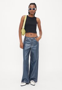 Black cropped tank top, light blue wide-leg jeans, white sneakers, and a bright green crossbody bag. Sunglasses with a thick white frame.