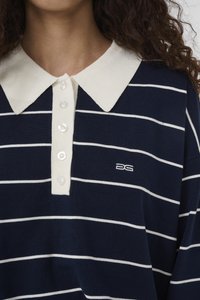 Kvinde bærer navyblå og hvide stribede polo-shirt med hvid krave og fem knapper, med en lille broderet DG-logo på brystet.