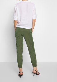 Vit linneöverdel med kort ärm i kombination med gröna byxor med elastisk midja och svarta klacksandaler. Outfiten har en avslappnad passform och en ledig design.