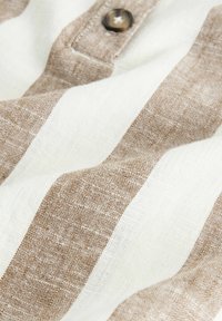 Beige ja valge triibuline linakiudkangas lähedalt, millel on nähtav riide külge õmmeldud nööp.