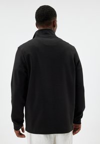 Black long-sleeve pullover shirt with a collar and soft texture, featuring a simple, seamless design and a relaxed fit.