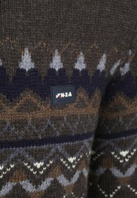 Bruine gebreide trui met geometrische patronen in crème, blauw en donkerblauw. Inclusief een zwart label met "N.Z.A" en merkdetails.