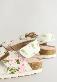 Weiße Sandalen mit floralem Muster in Pink und Grün, ausgestattet mit zwei verstellbaren Riemen und einer korkähnlichen Keilsohle. Weiche Innenauskleidung.
