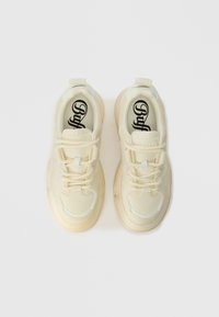 Kremfargede joggesko med teksturert overdel, tykk gummisåle og snøring. Har fremtredende logo på innersålen og lette aksenter.