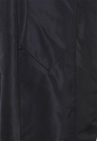 Černá látka s hladkým povrchem a viditelnými švy. Obsahuje šošolkovou kapsu v dolním levém rohu.