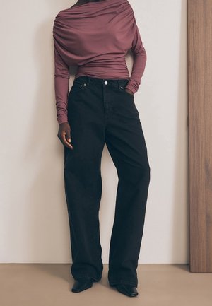 Osoba w marszczonej, wrzosowej bluzce z długim rękawem, wsuniętej w wysokowasniste, szerokie, czarne dżinsy oraz czarne buty z ostrym noskiem.