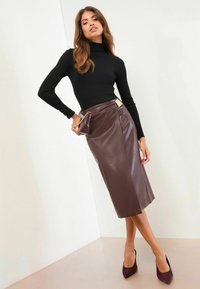 Dolcevita nero a coste, gonna midi in pelle marrone con spacco laterale, abbinata a scarpe con tacco bordeaux e una piccola borsa.