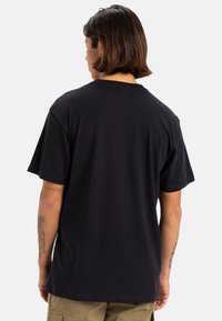 Camiseta de algodón negra de mangas cortas y cuello redondo, con un diseño liso en la parte posterior y corte relajado, mostrada desde la parte trasera.