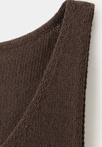 Tissu tricoté marron foncé en gros plan montrant deux sections texturées avec des motifs de tricot différents et un bord plié sur un fond clair.