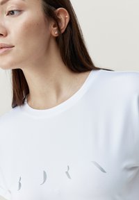 Witte t-shirt met een ronde halslijn en een reflectief grijs tekstontwerp. De stof ziet er glad uit, met een subtiele glans en een losse pasvorm.