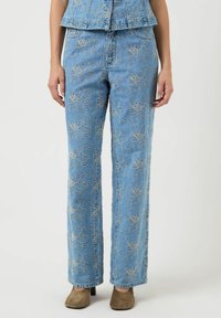 Niebieskie dżinsy z beżowym kwiatowym haftem, o prostym kroju, noszone z brązowymi butami na obcasie i dopasowaną haftowaną bluzką.