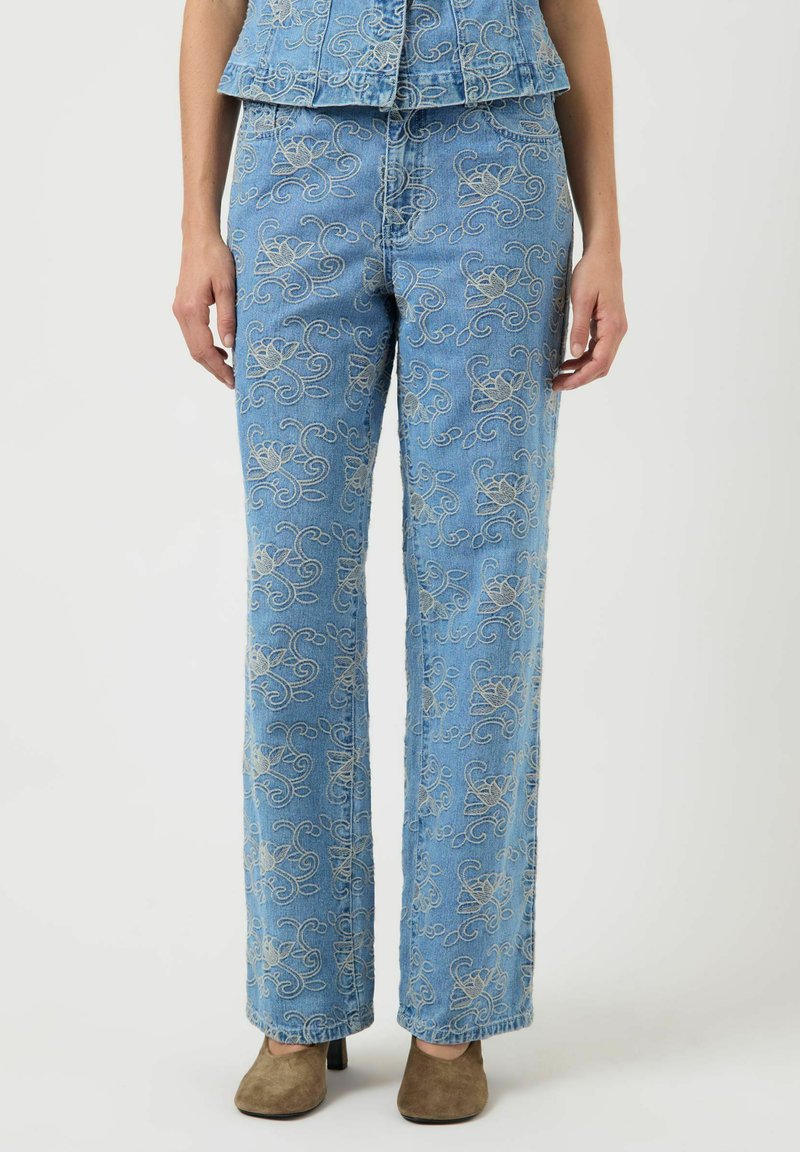 Niebieskie dżinsy z beżowym kwiatowym haftem, o prostym kroju, noszone z brązowymi butami na obcasie i dopasowaną haftowaną bluzką.