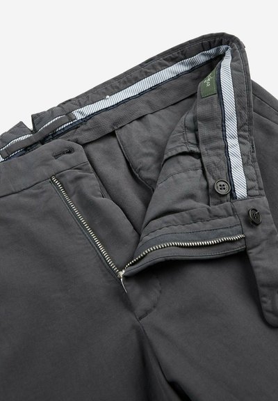 Pantalons gris avec une fermeture éclair, un bouton et une doublure rayée. Le tissu semble lisse avec une texture légèrement mate.