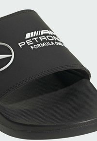 Crne natikače sa mekim gumenim trakama na kojima se nalaze bijeli tekst i logo, teksturirani uložak za stopala i ravni crni potplat.