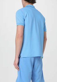 Polo shirt blu chiaro in tessuto morbido con colletto e maniche corte, abbinato a pantaloni corti blu chiaro coordinati. Fessure corte sui lati dell'orlo.