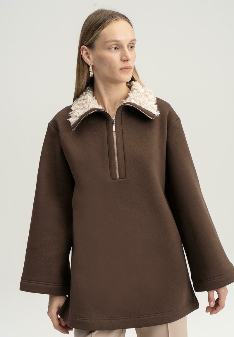 Felpa marrone con colletto con zip, dotata di una morbida fodera beige e ampie maniche a campana. Tessuto morbido senza pattern visibili.