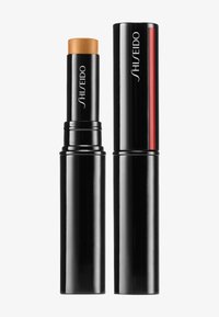 Fondotinta in stick Shiseido con un tappo dorato, racchiuso in un elegante tubo nero. Presenta una finitura lucida e un audace accento rosso sul lato.