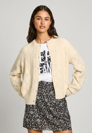 Stickad cardigan i ljus krämfärg med ett texturerat mönster, med rund hals, knappstängning och ribbade muddar, matchad med en blommig kjol.