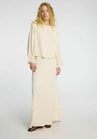 Conjunto de dos piezas en color crema que incluye una blusa de manga larga y una falda maxi con detalles de costura diagonal y una textura suave.