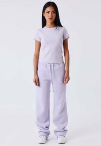 Camiseta ajustada de color púrpura claro con mangas cortas y logotipo bordado; combinada con pantalones de chándal sueltos púrpura claro con cinturilla elástica.