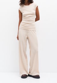 Top en tricot côtelé beige à manches courtes associé à un pantalon beige à coupe ample avec taille à cordon. Le modèle porte des chaussures à semelles chunky noires.