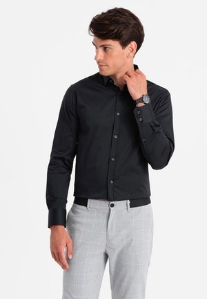 Schwarzes Langarmshirt mit spitzem Kragen und Knopfleiste, kombiniert mit hellgrauen karierten Hosen. Glatter Stoff und taillierte Passform.