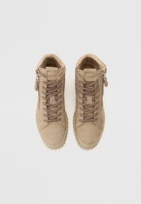 Baskets montantes en suede beige avec des lacets marron, fermeture éclair sur le côté et semelles en caoutchouc texturé, dotées d'un doublure douce au niveau du col.