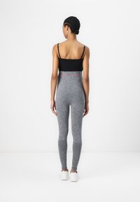 Leggings grigi con un design testurizzato, vita alta con un accento rosa, abbinati a una canotta nera e scarpe da ginnastica bianche.