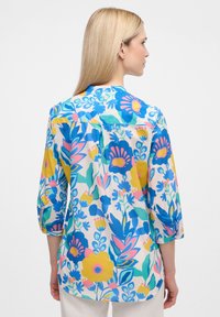 Blumenbluse in hellen Farben mit blau, pink und gelben Mustern. Hergestellt aus leichtem Stoff mit einer lockeren Passform und dreiviertel Ärmeln.