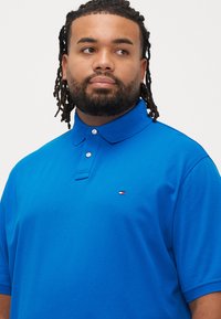 Blå poloshirt med struktureret stof, krave med to knapper og et lille logo på venstre bryst. Korte ærmer og afslappet pasform.