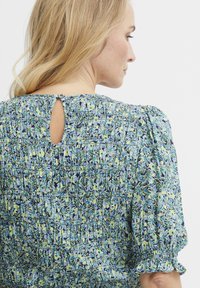 Blumenkleid mit blauem und grünem Muster, gerüschtem Oberteil, kurzen Puffärmeln und einem Schlitzdetail am Rückenausschnitt.