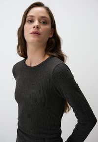 Top aderente a maniche lunghe realizzato in morbido tessuto a costine grigio scuro. Collo arrotondato, texture morbida, leggero lucido, che mette in risalto le curve del corpo.