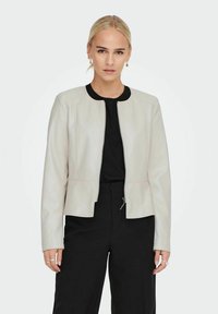 Jachetă din piele gri deschis, cu fermoar în față, guler rotund și croială structurată. Purtați-o peste un top negru și asortați-o cu o pereche de pantaloni negri.