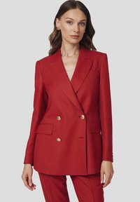Czerwona marynarka dwurzędowa z teksturowanej tkaniny, z złotymi guzikami, klapami oraz bocznymi kieszeniami. Dopasowany krój, długie rękawy.