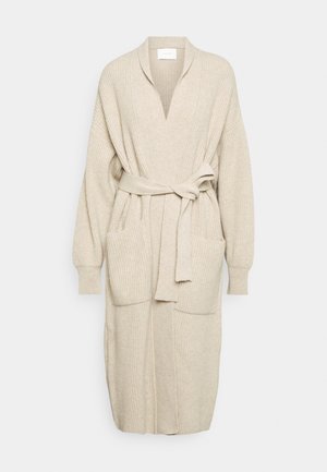 Lang beige strikket cardigan med frontlommer, bælte i taljen og lange ærmer, vist på en ensfarvet lys baggrund.