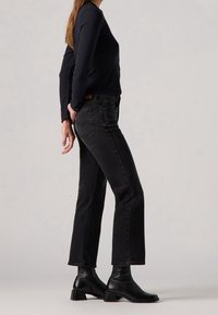 Jeans en denim noir avec une coupe droite, dotés d'une taille mi-haute et de poches arrière discrètes, associés à des bottines noires.