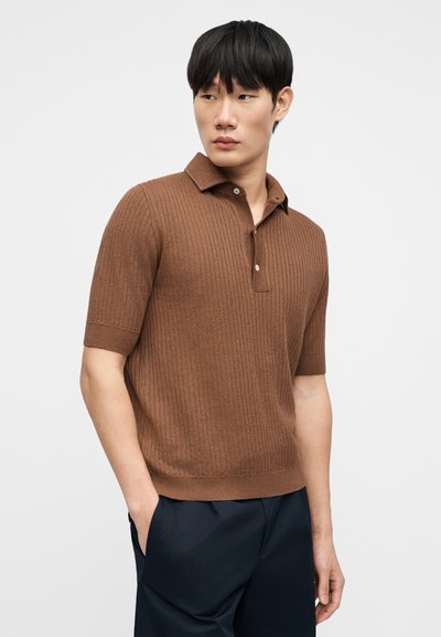 Polo marron côtelé avec un col et des manches courtes, fabriqué à partir d'un tissu texturé. Présente une patte à trois boutons.