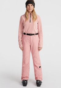 Light pink fleece top with a half-zip and long sleeves; matching pink pants; black belt; black ski boots; textured fabric and accents visible.