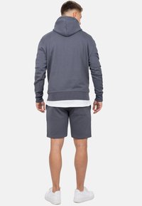Grijze hoodie met een trekkoord, ribbelmanchetten en -zoom, gecombineerd met bijpassende shorts. Het model draagt witte sneakers en een gelaagd wit shirt eronder.