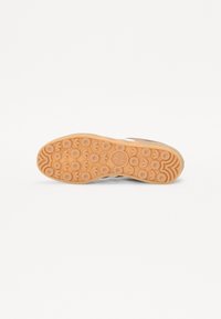 Guma podešev boty v světlé tan barvě s oblíbenými kulatými vzory pro grip a centrálním logem značky. Celkový tvar je plochý s zaoblenými okraji.